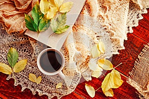 Autumn, fall leaves, hot steaming cup of coffee and a warm scarf on wooden table background. Seasonal, morning coffee