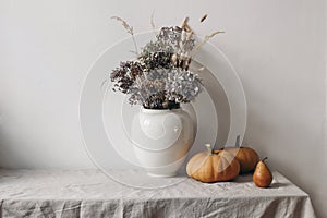 Autumn, fall still life. Big ceramic vase with dry hydrangea flowers, grass boho bouquet. Orange pumpkins and pear fruit