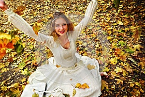 Autumn fashion dress woman sitting fall leaves city park outdoor.