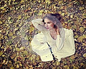 Autumn fashion dress woman sitting fall leaves city park outdoor.