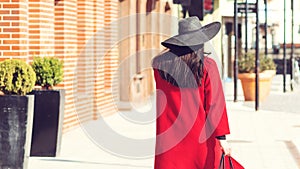 Autumn fashion. Elegant woman in red coat and stylish black hat, with trendy bag walking in city. Shopping day, great sales.