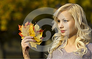 Autumn Fashion Girl. Blonde beautiful young woman with yellow maple leaves in hand. Outside.