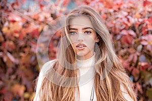 Autumn fashion. Pretty tenderness model looking at camera. Cheerful woman with long hair on red maple leaf outdoors in