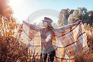 Autumn fashion. Young woman wearing stylish poncho, cap outdoors raising hands. Clothing and accessories