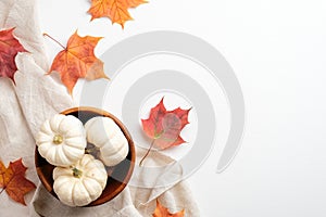 Autumn flat lay composition. Beige fabric, colorful maple leaves and bowl with pumpkins on white background. Top view. Autumn fall