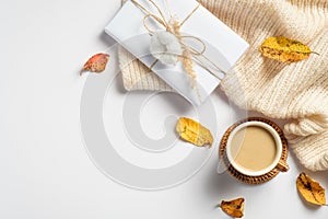 Autumn flat lay composition with knitted scarf, gift box, morning coffee cup, dry leaves on white background. Cozy home desk,