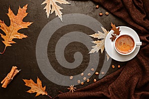 Autumn flat lay. Cup of coffee, brown pashmina scarf, autumn leaves, cinnamon sticks, coffee beans on black background