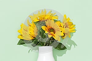 Autumn flower of sunflower in white vase on mint colored background. Natural bright yellow blossom with green leaves
