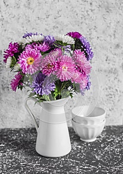 Autumn flowers asters in a white pitcher on a light background.