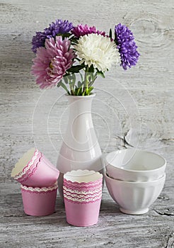 Autumn flowers asters in a white vase, ceramic bowls and paper molds for baking cakes, still life in vintage style