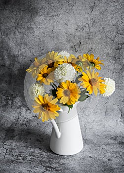 Autumn flowers yellow and white dahlias bouquet in a vintage white metal jug on a gray background, front view