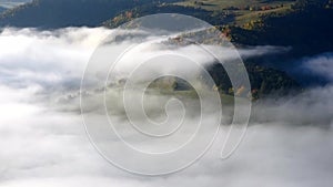 Autumn fog floats over the landscape among the trees.