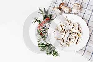 Autumn food arrangement. Composition of whole and sliced porcino mushrooms, ceps on plate. Rowan berries, leaves, fir photo