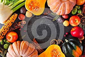 Autumn food frame with pumpkins, apples, squash and a variety of vegetables over a dark stone background