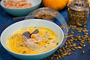 Autumn food - pumpkin soup with cream, shrimps and seeds in bowls on table. Served for dinner. View from above