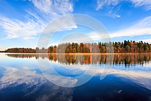 Autumn forest and blue sky reflect on the smooth surface of the lake. Panorama, wide angle, fish eye lens.