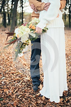 In the autumn forest the bridegroom embraces the bride, the bride holds a bouquet