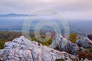 Autumn forest landscape among large rocks with view of mountain misty valley and colorful autumn forest.