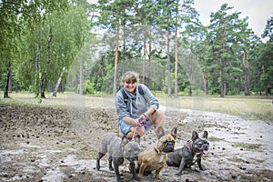 In the autumn forest  a lgirl plays with three French bulldogs