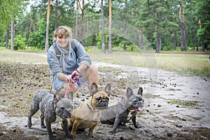 In the autumn forest  a lgirl plays with three French bulldogs