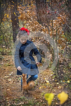 In the autumn forest, a little girl feeds a squirrel with nuts