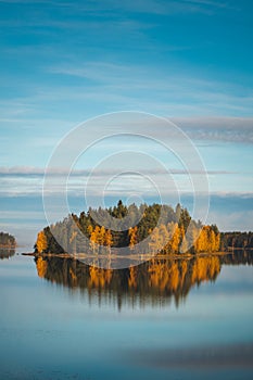 Autumn forest on a small island coloured in autumn colours. Reflection of orange and green trees in the lake around the town of