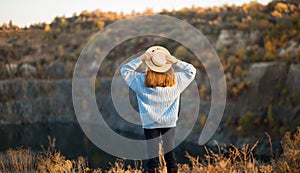 Autumn girl in blue sweater and hat standing backwards and admire nature lake view. Autumn forest colors with girl back view