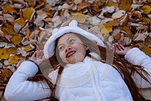 Autumn girl playing in city park. Portrait of an autumn woman lying over leaves and smiling outside in fall forest. Beautiful ener
