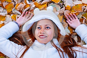 Autumn girl playing in city park. Portrait of an autumn woman lying over leaves and smiling outside in fall forest. Beautiful ener