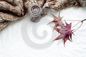 Autumn greeting card mockup scene with maple leaves, scented candle and plaid. White tablecloth background.Top view, flat lay,