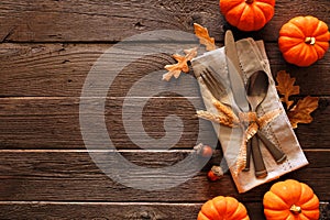 Autumn harvest or thanksgiving table scene with silverware, napkin, leaves and pumpkin border against a rustic wood background