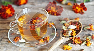 Autumn healing background. Folk medicine Glass of herbal tea with marigold flowers on wooden ancient background with dried flowers