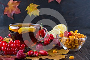 Autumn healthy beverages concept. Cup of tea with autumn berries sea buckthorn, viburnum, rose hip, rowan and fall leaves. Drink