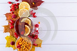 Autumn healthy beverages concept. Cup of tea with autumn berries sea buckthorn, viburnum, rose hip, rowan and fall leaves. Drink