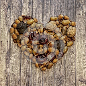 Autumn heart shape by various nuts and acorns on a wooden background