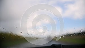 Autumn highway on a rainy day - defocused background. Moving waterdrops in the wipers of the windshield