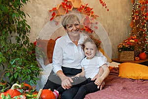Autumn holiday grandmother and granddaughter at home on the bed with pumpkins and falling leaves, lifestyle happy family