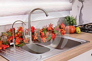 Autumn kitchen interior. Red and yellow leaves and flowers in the vase and pumpkin on light background