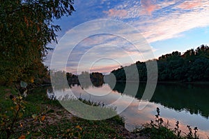 Autumn landscape, beautiful sunset and bright colorful forest in the evening, trees near river and blue sky