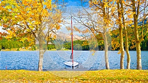 Autumn landscape on the lakeside. Trees with yellow leaves. A boat on the shore of a mountain lake. Natural landscape in autumn ti