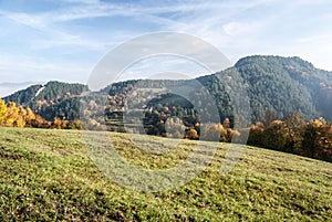 Autumn landscape with meadow, colorful trees, hills and blue sky with clouds