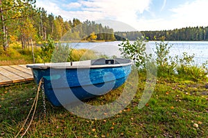 Autumn landscape, an old blue boat lies on the shore of a forest lake. The boat is pulled ashore for the winter for safety