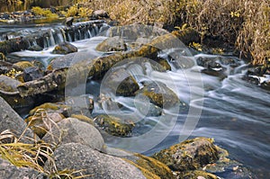 Autumn landscape with a river flowing smoothly between the boulders