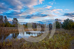 Autumn landscape with riverbank at sunset. Wonderful nature, beautiful natural background. Sky with clouds is reflected