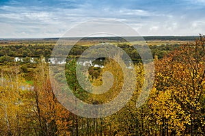 Autumn landscape: trees with yellow leaves grow on the banks of a cold autumn river amid dark skies