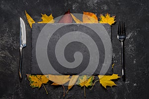 Autumn layout with still life of black stone tray, autumn leaves, fork and knife.