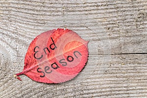 Autumn leaf with the inscription END SEASON, on the old wooden background