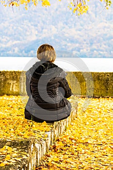 Autumn leaves fallen on standing alone woman on the autumn alley. Autumn landscape, orange foliage in a park in Orsova, Romania,