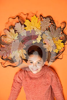 Autumn leaves are falling down. Happy girl wear colorful leaves in long hair. Creating hairstyle using fall leaves