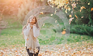 Autumn leaves falling on happy young woman in forest. Portrait of very beautiful girl in fall park